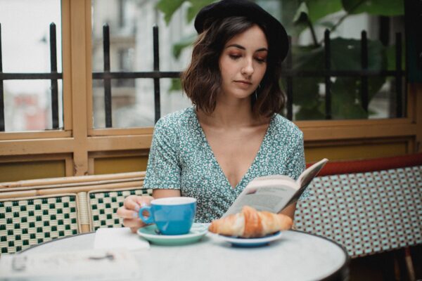A young woman enjoys reading a book indoors with coffee and a croissant on a relaxing day.